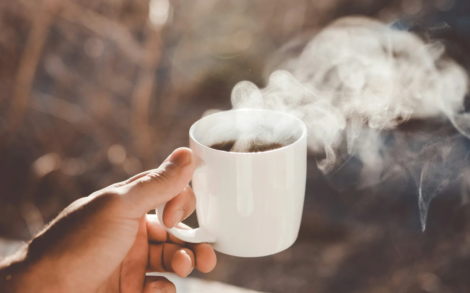 Hand hält einen dampfenden Kaffeebecher