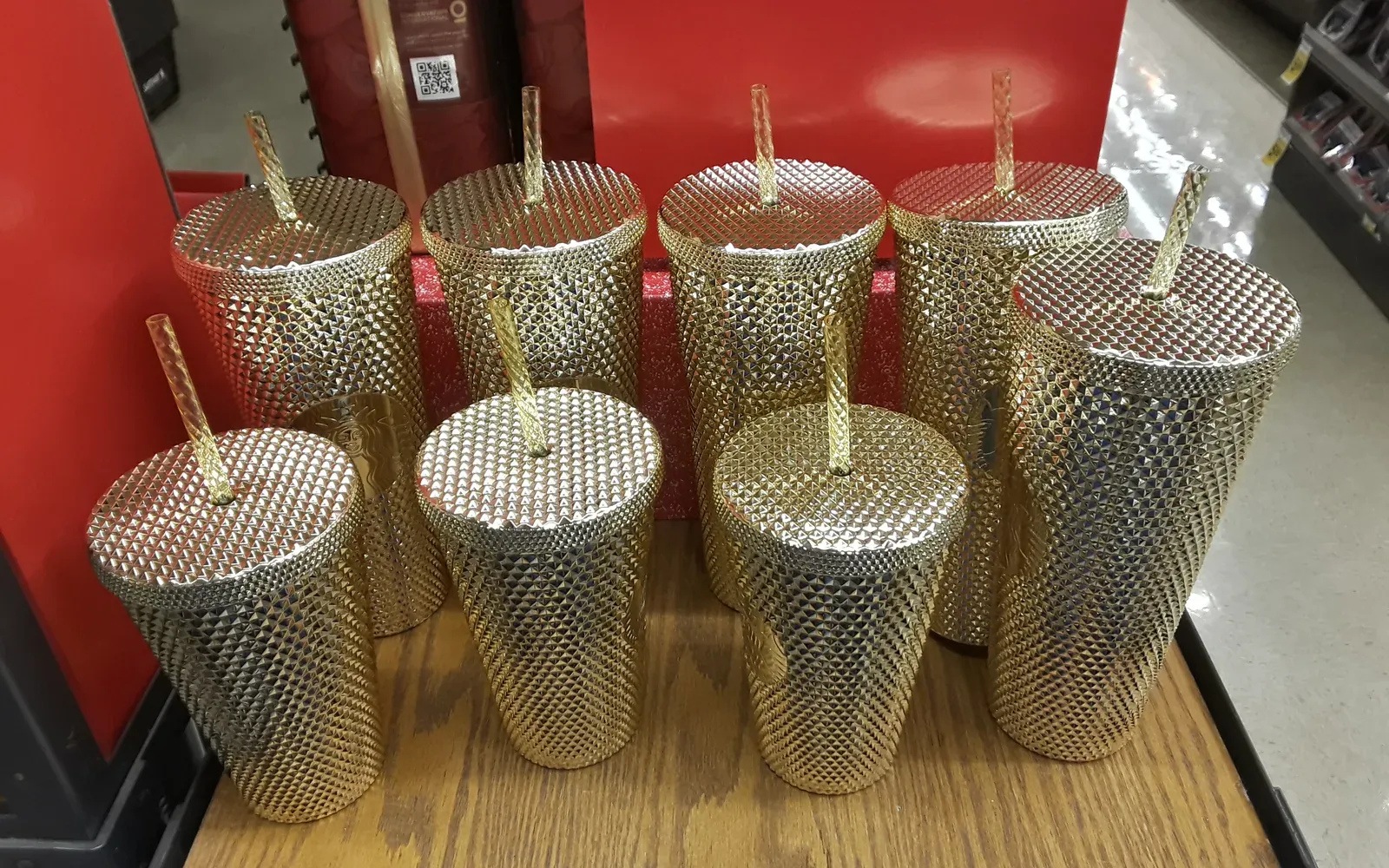 Goldene Starbucks Cold Cups mit Nietenoptik und Strohhalm in einem Verkaufsregal