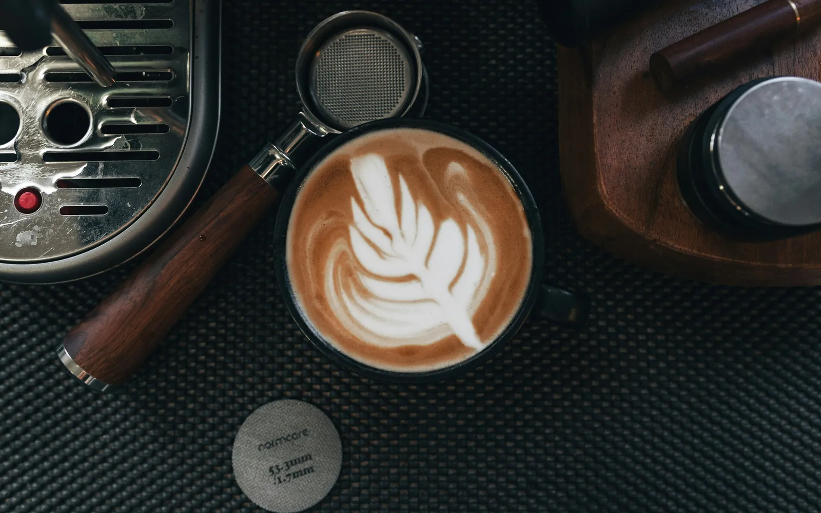 Latte Art in einer schwarzen Tasse neben Siebträger und Espressomaschine, Draufsicht