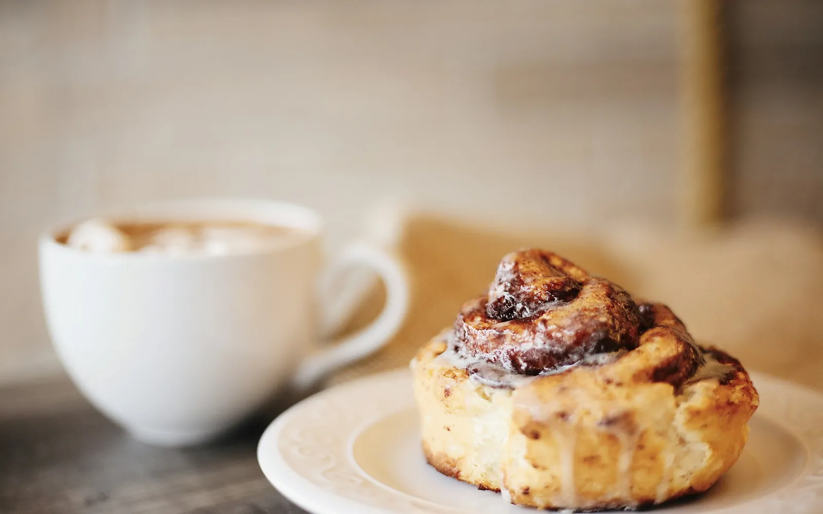 Zimtschnecke mit Zuckerguss auf einem Teller neben einer Tasse Kaffee